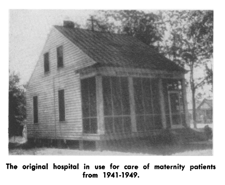 A small white wooden house with a cross on the top. The caption says it is the original hospital used for the care of maternity patients from 1941-1949.